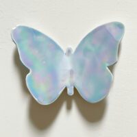 A Custom Butterflies pearlescent ornament in pastel blue, purple, and green hues is mounted on a plain white surface.